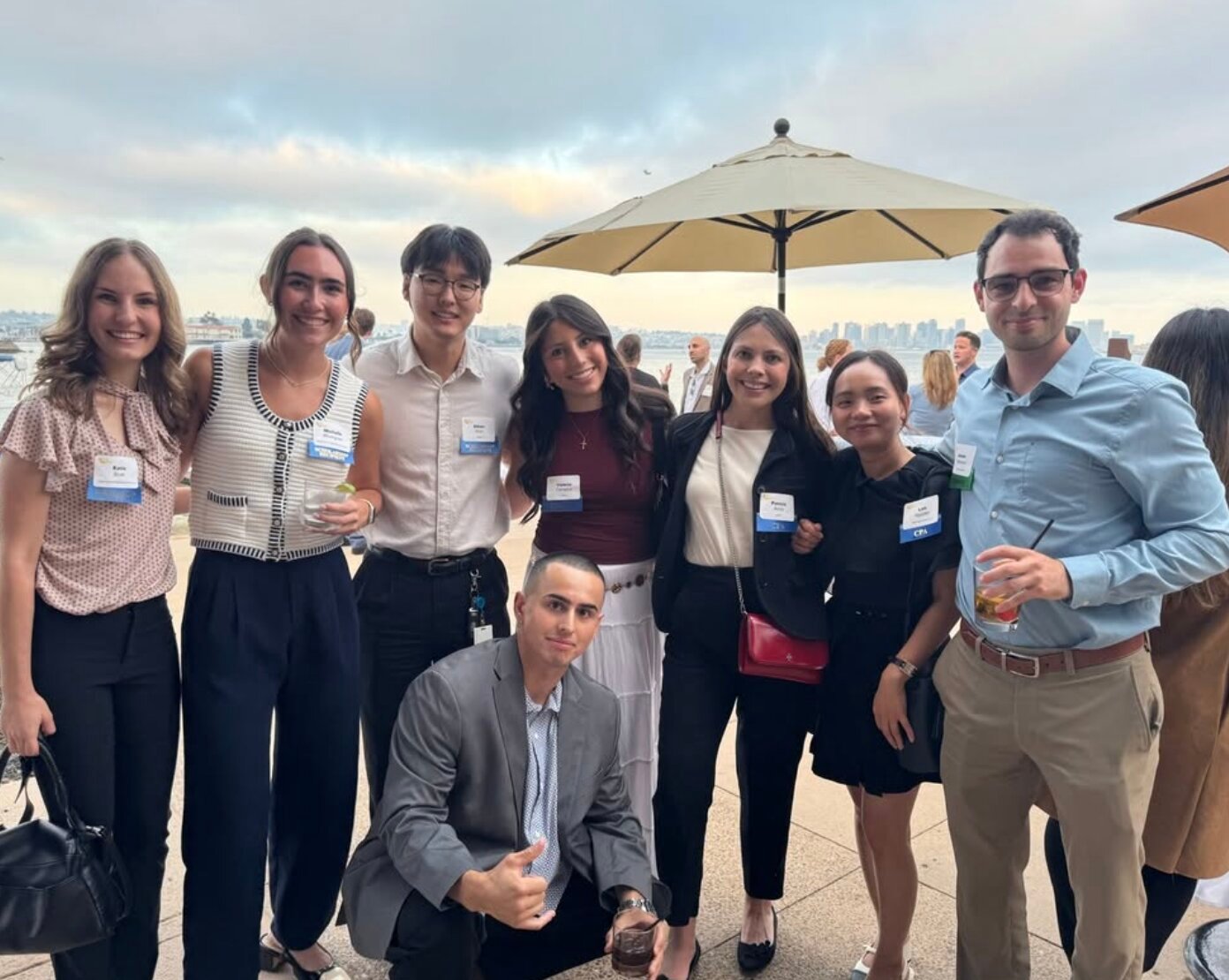 A group of 8 accounting professionals smile at the camera at a CalCPA San Diego chapter event with a view of downtown San Diego in the distant background