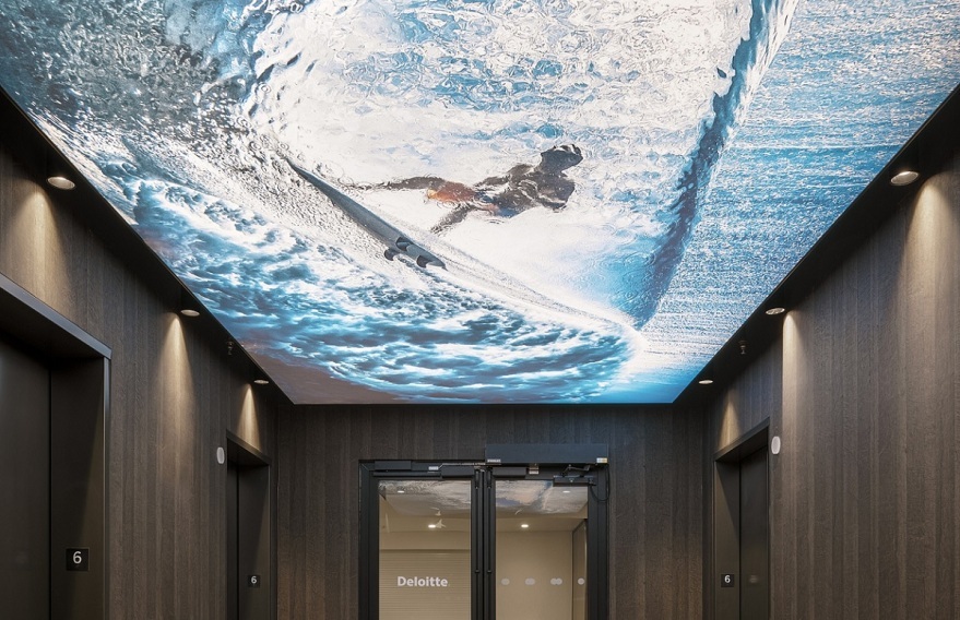 Hallway of Deloitte San Diego office, which has dark wooden panels and a ceiling covered by a blown up photo of a surfer on a wave